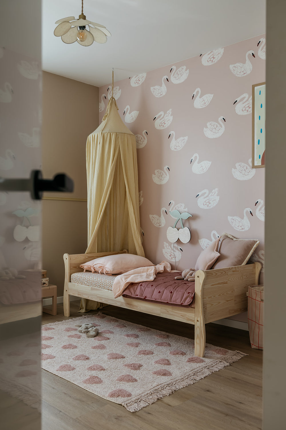 Vloerkleed Rosy Hearts rechthoek met roze hartjes voor een houten kinderbed met gele hemel en zwanenbehang