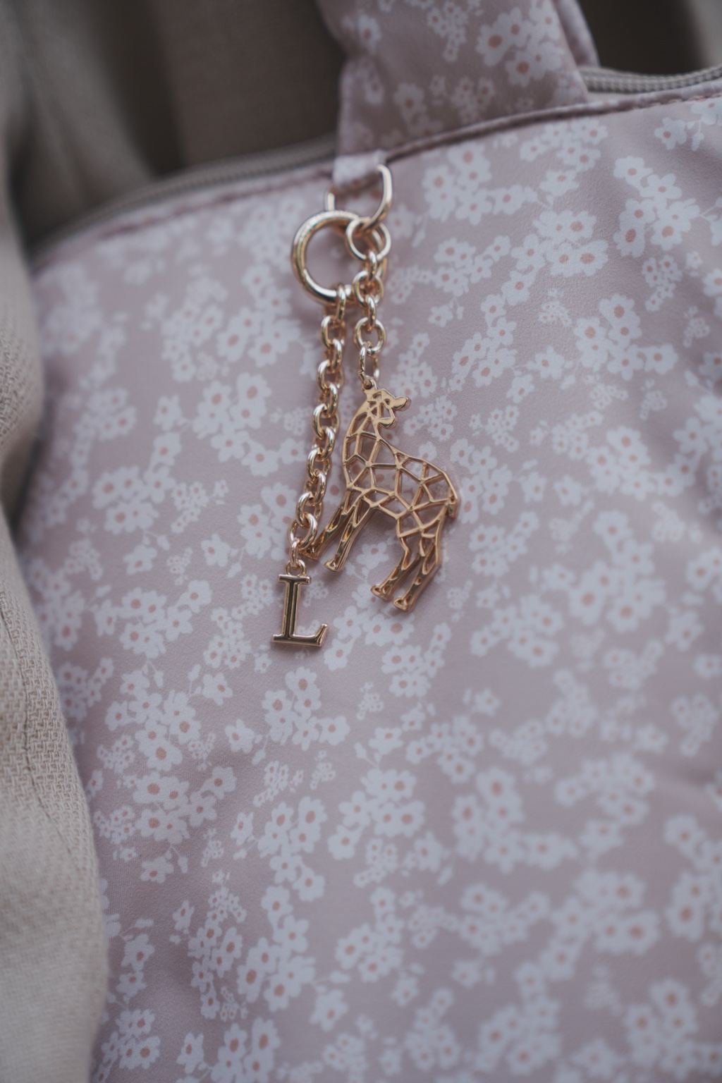 Gouden Love by Lily sleutelhanger met initiaal, bevestigd aan een lila luiertas met bloemenprint