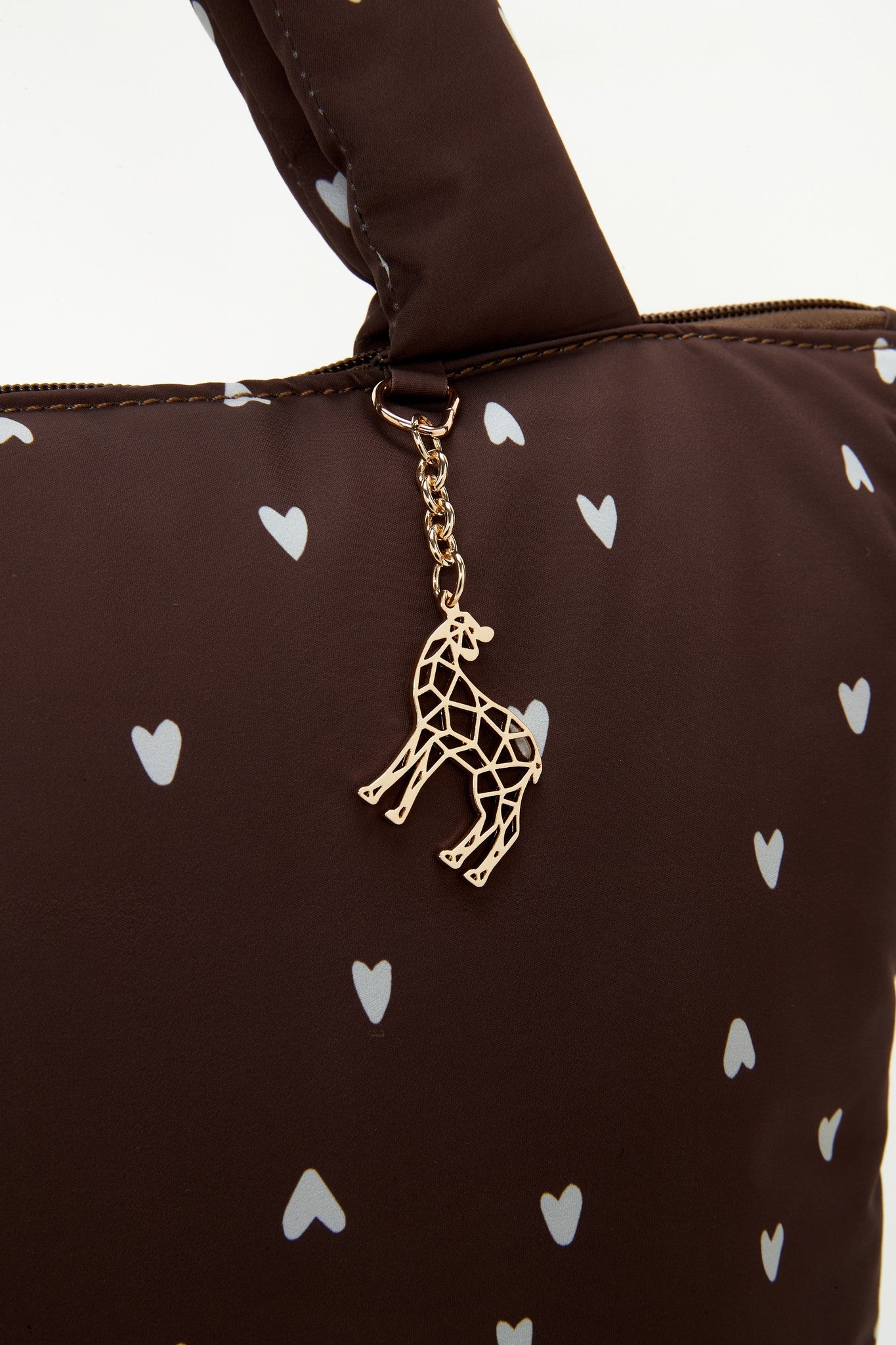 The Lily Tote luiertas van Love by Lily in Deep Amour hartjesprint, close-up van het gouden giraffe-hangertje aan de hengsel